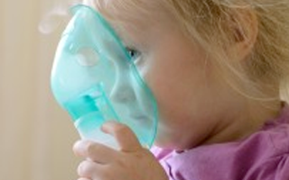 A child holds a plastic nebulizer mask, made from polycarbonate plastics, in front of her face.