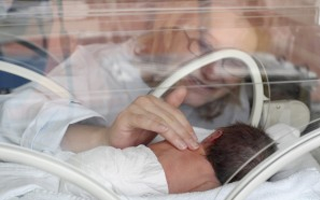 A woman touches an infant in neonatal incubator, just one example of polycarbonate plastic in medical devices.