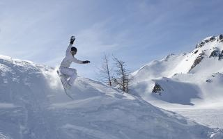 A snowboarder in white snowsuit and black helmet descends a mountain.